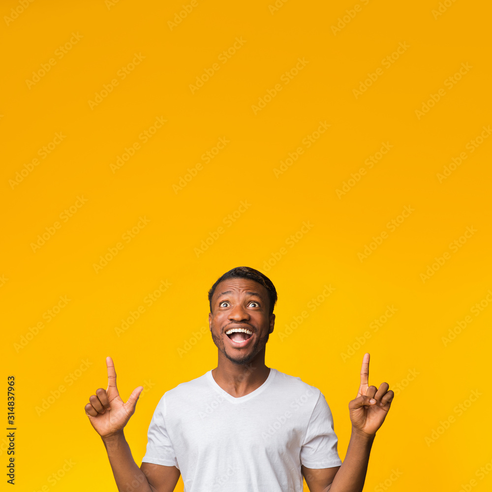 Millennial Guy Pointing Fingers Upward In Excitement Over Yellow Background