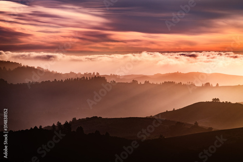 Fototapeta Naklejka Na Ścianę i Meble -  Sunset view of layered hills and valleys in Santa Cruz mountains; clouds covering the sky and the Pacific Ocean; San Francisco bay area, California