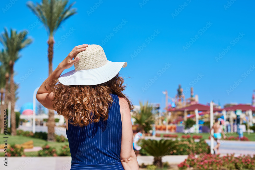 Fototapeta premium Woman in hat and blue dress go for a walk in the hotel resort