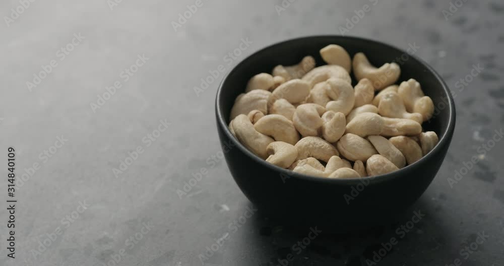 Slow motion handheld shot of cashew nuts in black bowl on terrazzo countertop Slow motion handheld shot of cashew nuts in black bowl on terrazzo countertop
