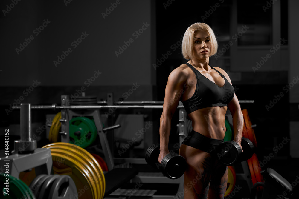Naklejka premium Female bodybuilder posing with dumbbells.