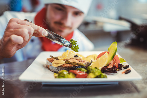 Proud chef garnishing an almost finished dish in the restaurant with leave photo