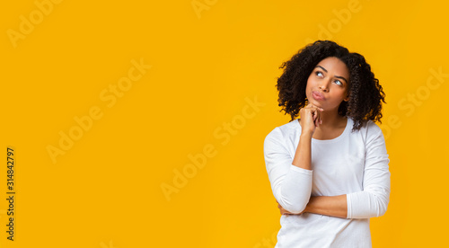 Doubtful afro girl thinking about something over yellow background photo