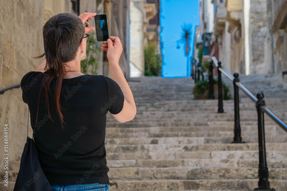 Naklejka premium Traveler woman taking photo with mobile phone of Medieval narrow street with stairs in Valletta, Malta.