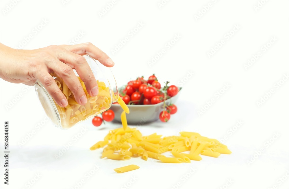 a hand pours pasta from a jar and cherry tomatoes with a white background