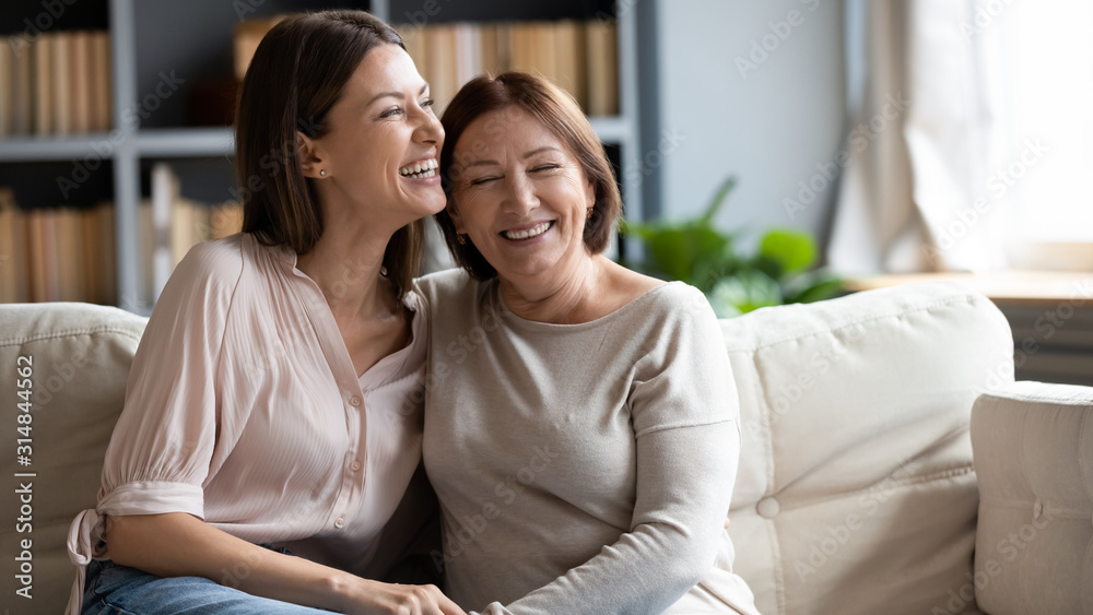 Happy senior mother and adult daughter laugh relaxing at home