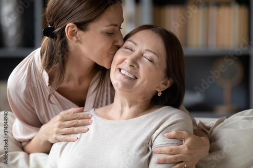 Loving adult daughter kiss senior mother relaxing together