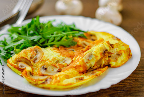 Omelet with mushrooms and arugula salad in white plate on wooden table background.