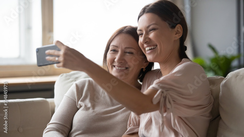 Smiling adult mother and daughter posing for selfie on cell