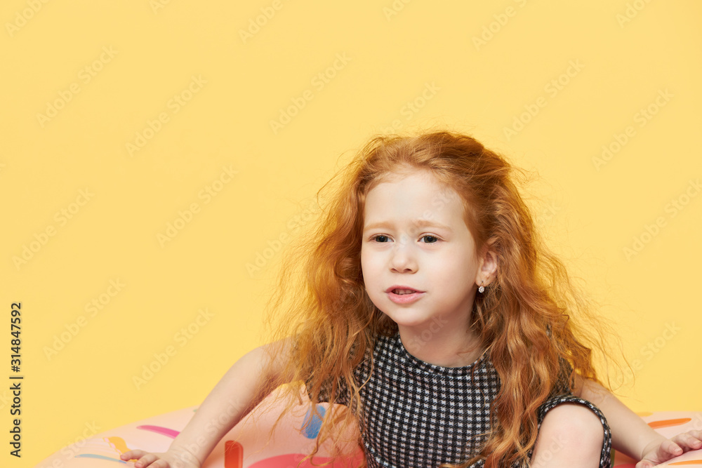 Games, leisure, activity and water sports concept. Isolated shot of pretty Caucasian with long ginger hair sitting on pink swimming ring going to beach posing against yellow background with copy space