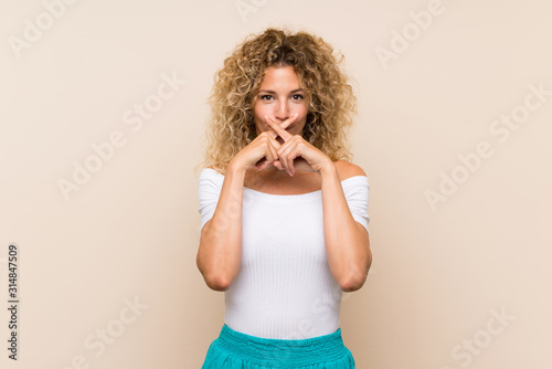 Young blonde woman with curly hair over isolated background showing a sign of silence gesture