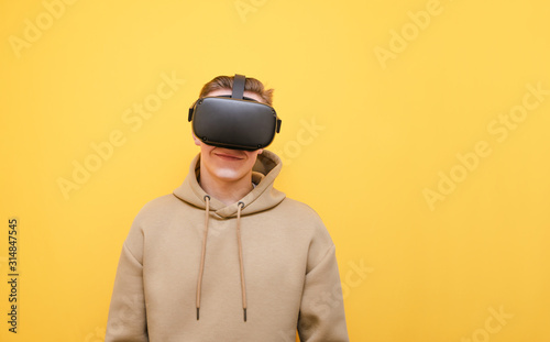 Positive VR gamer isolated on yellow background, wearing a helmet on his head and smiling while looking into the camera. Young man playing video games in virtual reality.