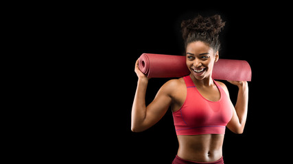 Cheerful black girl in sportswear holding yoga mat