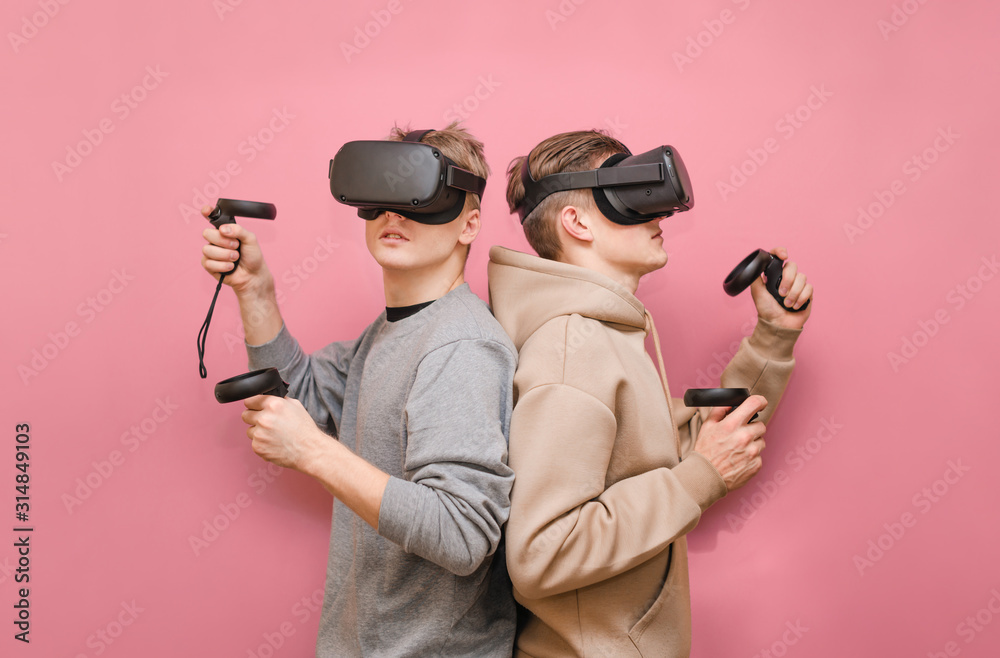 Two young men in VR helmets on their heads stand side by side on a pink