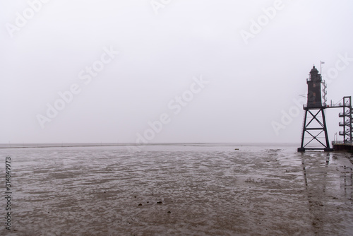 old lighthouse with low tide and fog at the northsea