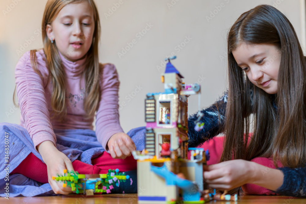 Fototapeta premium Two little sisters are playing children's constructor at home. selected focus