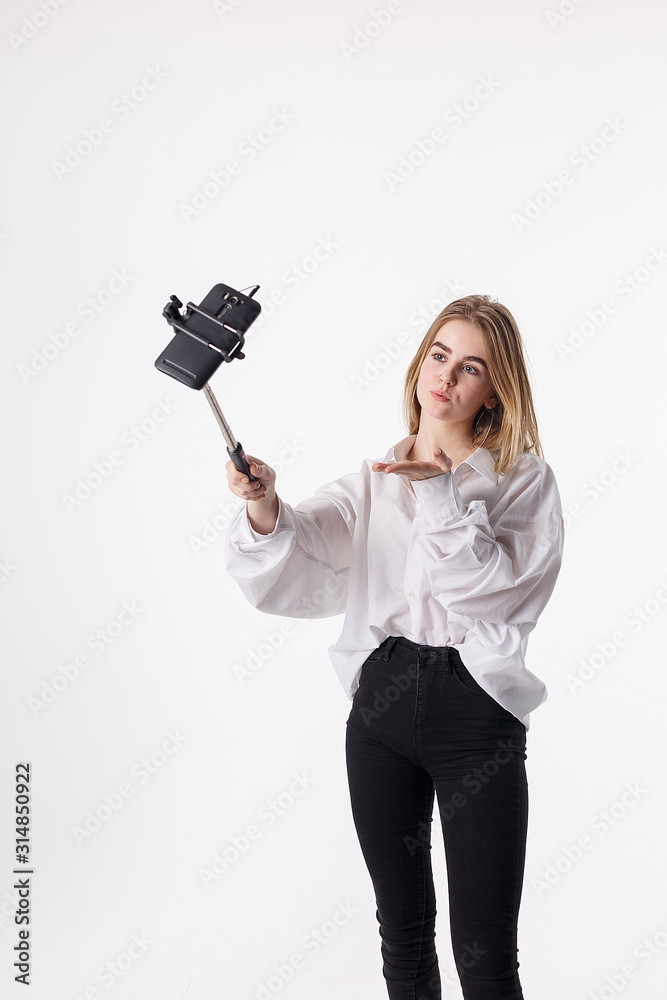 happy girl makes self portrait with smartphone attached to selfie stick. young pretty blond female with long hair sending air kiss, using cell phone isolated on white background. teen communication happy girl makes self portrait with smartphone attached to selfie stick. young pretty blond female with long hair sending air kiss, using cell phone isolated on white background. teen communication