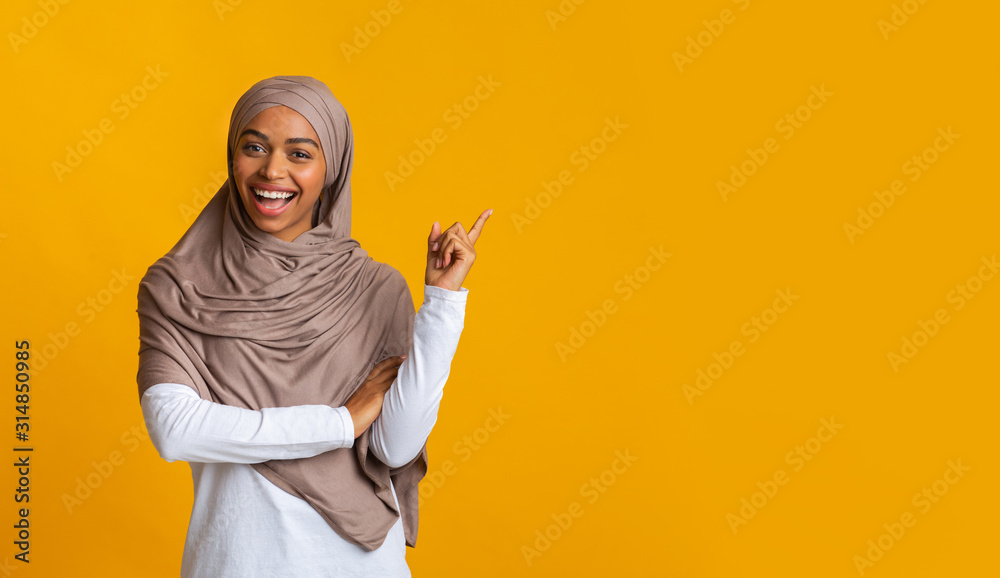 Cheerful afro muslim girl in hijab pointing aside at copy space Cheerful afro muslim girl in hijab pointing aside at copy space