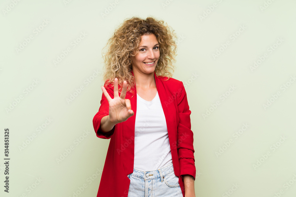 Young blonde woman with curly hair over isolated green background happy and counting three with fingers Young blonde woman with curly hair over isolated green background happy and counting three with fingers