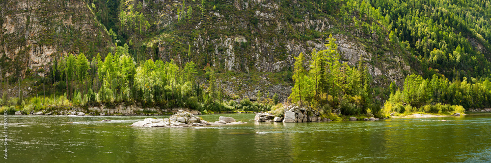 Steep mountain bank covered by taiga forest and rocky islands on the Small Yenisei river in sunny summer day. Siberia, Russia.