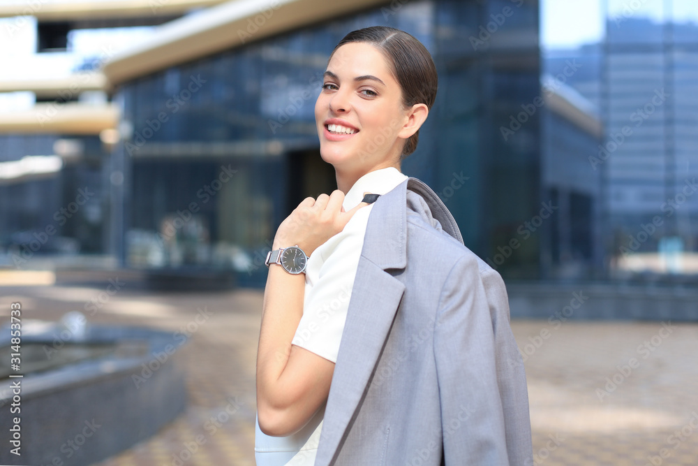 Smiling business woman standing with a jacket over her shoulder near office building. Smiling business woman standing with a jacket over her shoulder near office building.