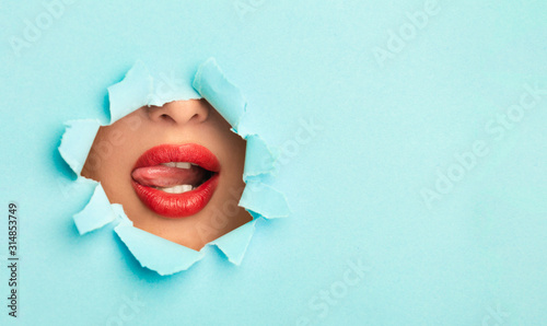 Woman with red lips playing with tongue in turquoise paper hole