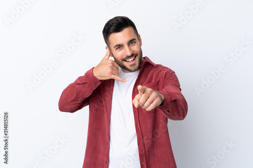 Young handsome man with beard wearing a corduroy jacket over isolated white background making phone gesture and pointing front