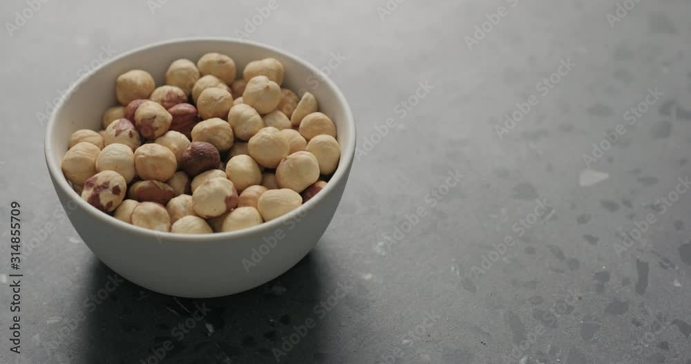 Slow motion handheld shot of roasted hazelnuts in white bowl on terrazzo countertop Slow motion handheld shot of roasted hazelnuts in white bowl on terrazzo countertop