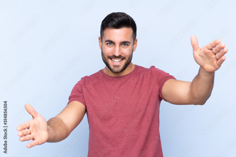Fototapeta premium Young handsome man with beard over isolated blue background presenting and inviting to come with hand