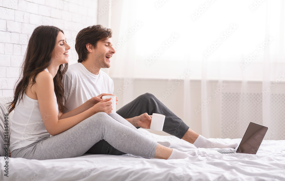 Happy spouses watching video on laptop and laughing in bed Happy spouses watching video on laptop and laughing in bed