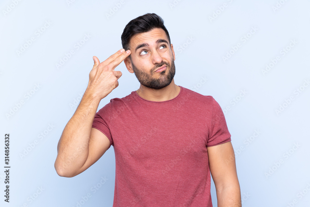 Young handsome man with beard over isolated blue background with problems making suicide gesture Young handsome man with beard over isolated blue background with problems making suicide gesture