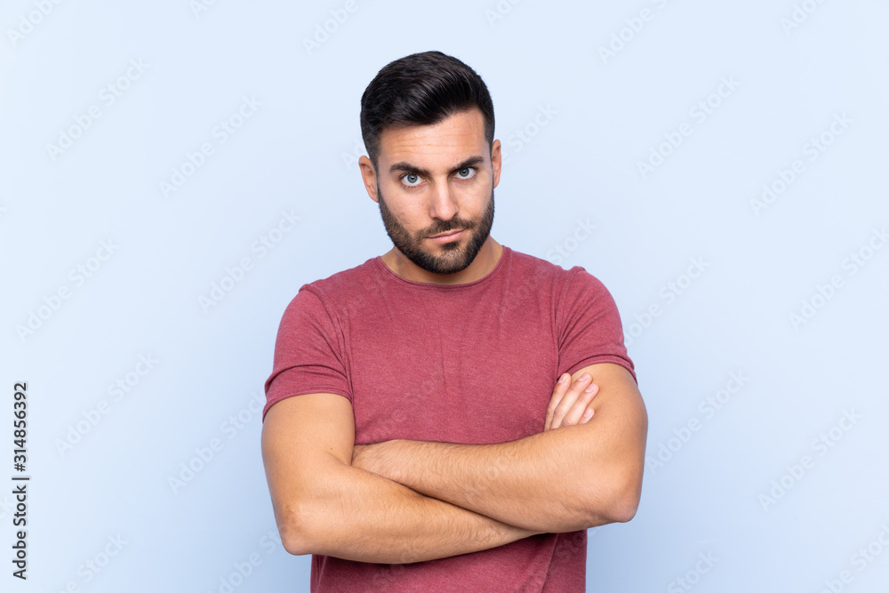 Young handsome man with beard over isolated blue background feeling upset Young handsome man with beard over isolated blue background feeling upset
