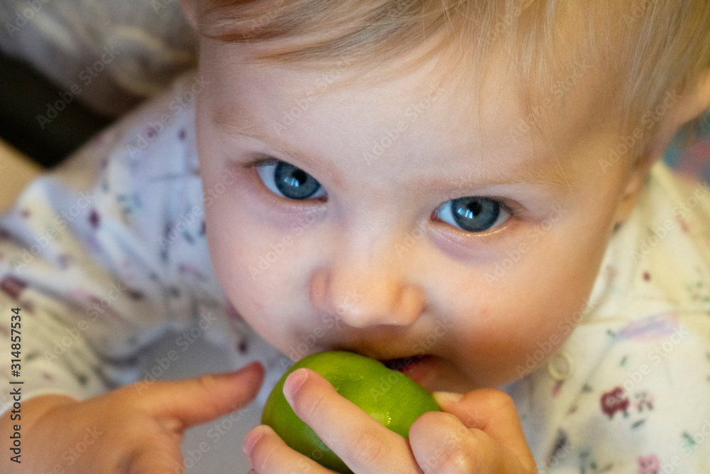 a little girl with blond hair with a green tomato in her hand