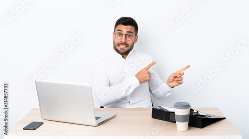 Young businessman in a workplace frightened and pointing to the side