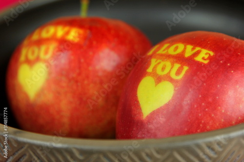Two Red Apple with text I LOVE YOU in a black clay bowl on red background. I love you apple. Apple for Valentine's Day