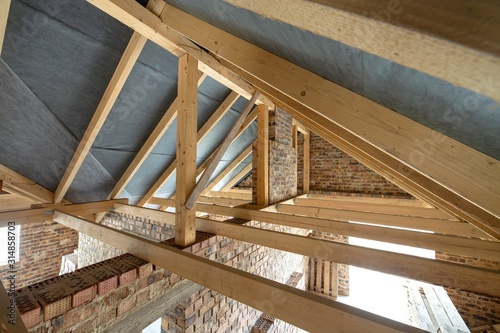 Attic space of a building under construction with wooden beams of a roof structure and brick walls. Real estate development concept.