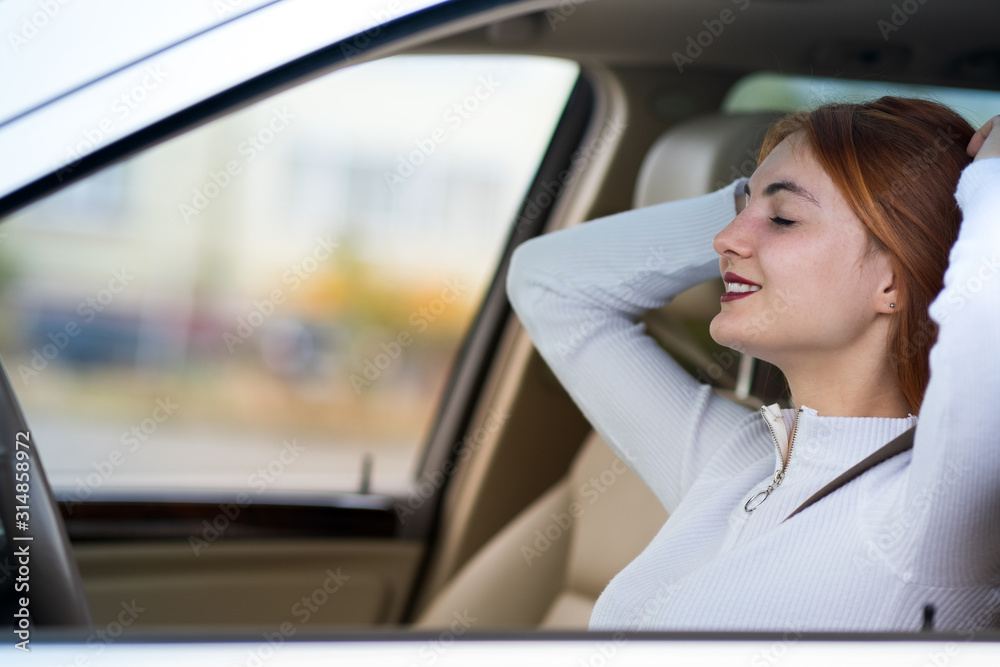 Young redhead woman driver fastened by seatbelt resting in a car smiling happily.