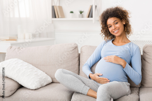 Happy pregnant woman sitting on sofa and caressing her belly