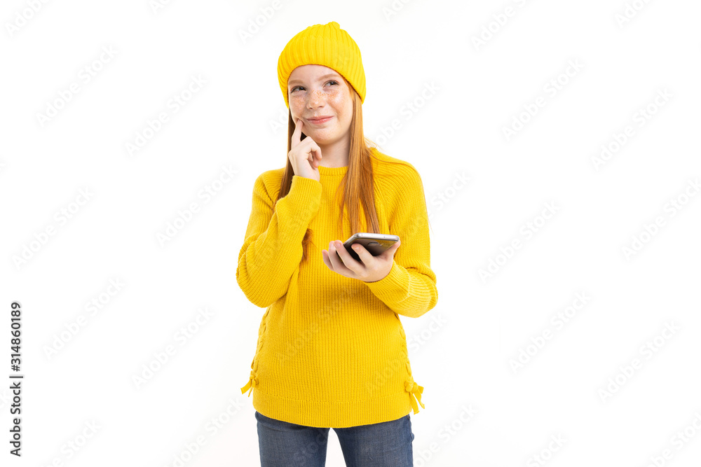 Happy teenager girl with red hair, yellow hoody and trousers communicate with phone and smiles isolated on white background Happy teenager girl with red hair, yellow hoody and trousers communicate with phone and smiles isolated on white background
