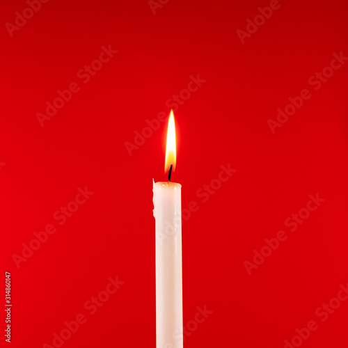 Burning candle on a red background. Square image.