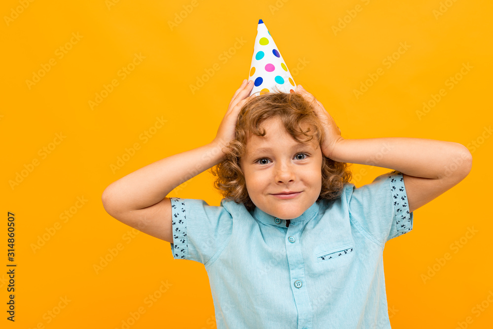 Little boy with curly hair in blue shirt and shorts is happy because have b-day isolated on yellow background Little boy with curly hair in blue shirt and shorts is happy because have b-day isolated on yellow background