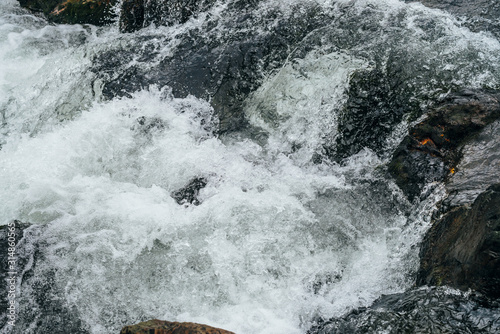 Full frame nature background of water riffle of mountain river. Powerful water stream of mountain creek with rapids. Natural textured backdrop of fast flow of mountain brook. Rapids texture close-up.