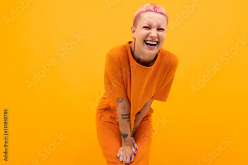 girl with pink hair and a pierced face dressed in a loose orange dress on a yellow background