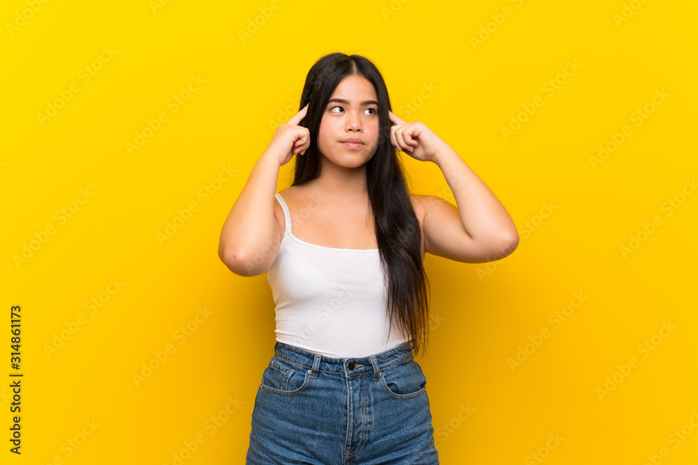 Young teenager Asian girl over isolated yellow background having doubts and thinking Young teenager Asian girl over isolated yellow background having doubts and thinking