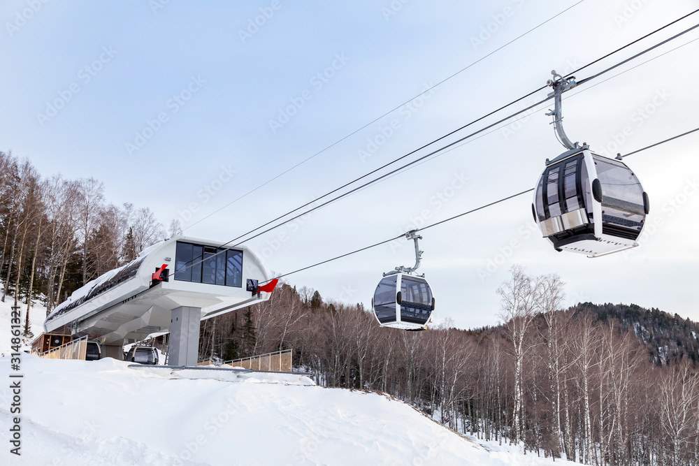 Upper passenger disembarkation point of a gondola cableway with a booth suspended on a rope on a background of mountains on winter sunset. Ski resorts and snowboarding. Upper passenger disembarkation point of a gondola cableway with a booth suspended on a rope on a background of mountains on winter sunset. Ski resorts and snowboarding.
