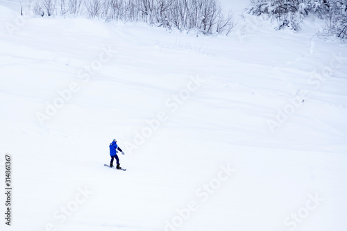 A man snowboarder slides down the mountain over white snow in a sports tourist base Turquoise Katun. Seasonal sports.