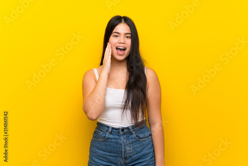 Young teenager Asian girl over isolated yellow background with surprise and shocked facial expression