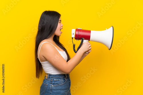 Young teenager Asian girl over isolated yellow background shouting through a megaphone