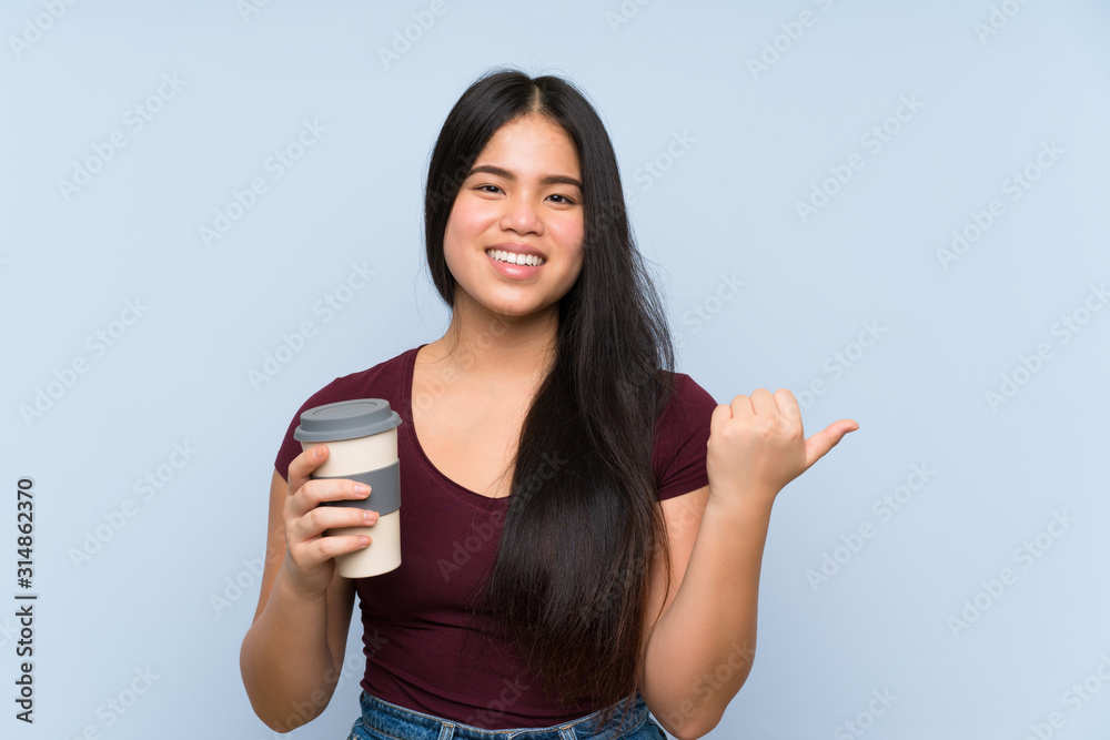 Young teenager Asian girl holding a take away coffee pointing to the side to present a product Young teenager Asian girl holding a take away coffee pointing to the side to present a product