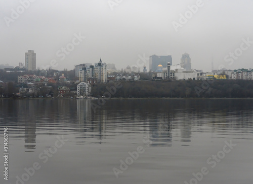 Cloudy winter day in the city. Houses, trees and bridges in the city are reflected in the water of the river on a cloudy day at the beginning of winter. © Светлана Горбань